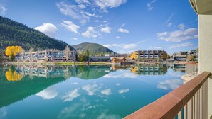 A lakeside view with buildings reflecting on the water, a wooden deck, and a mountain in the background. - Keystone Lake Haven: Heated Pool & Ski Shuttle! (Keystone)