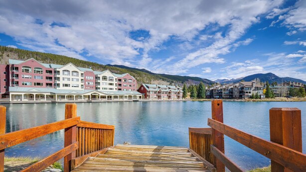 A wooden dock leading to a waterfront hotel with multiple buildings, a calm lake, and mountains in the background. - Keystone Lake Haven: Heated Pool & Ski Shuttle! (Keystone)