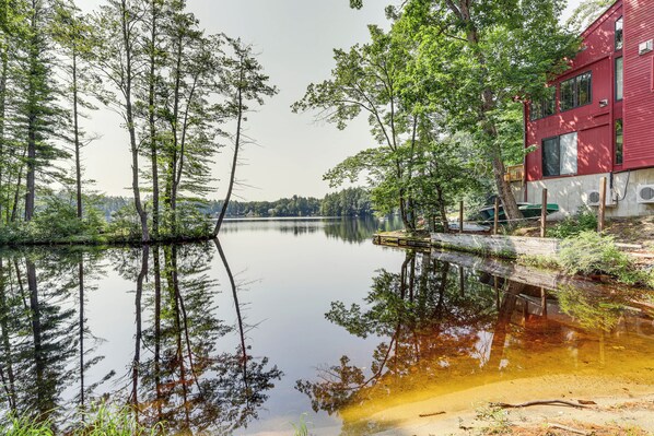 Une propriété au bord du lac, avec un bâtiment rouge qui se reflète dans l’eau, ainsi que les arbres et la surface calme du lac.