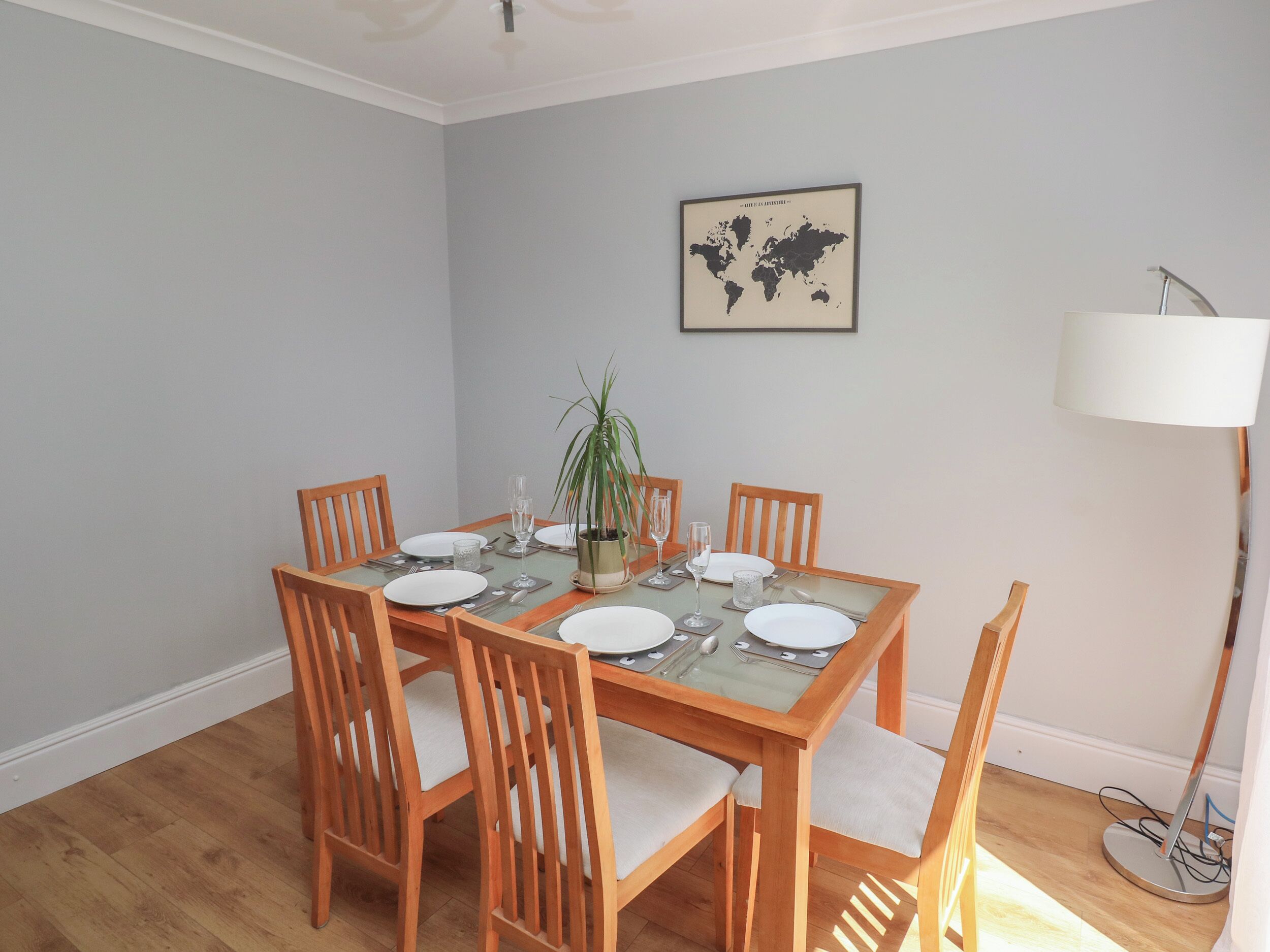 A dining area with a glass-top table, wooden chairs, and a world map on the wall.