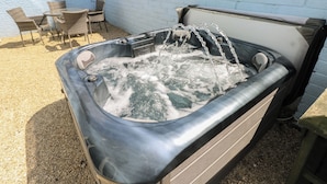 A hot tub with water flowing, surrounded by a white wall and a gravel area.