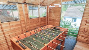 A wooden foosball table in a room with large windows and a view of a house.