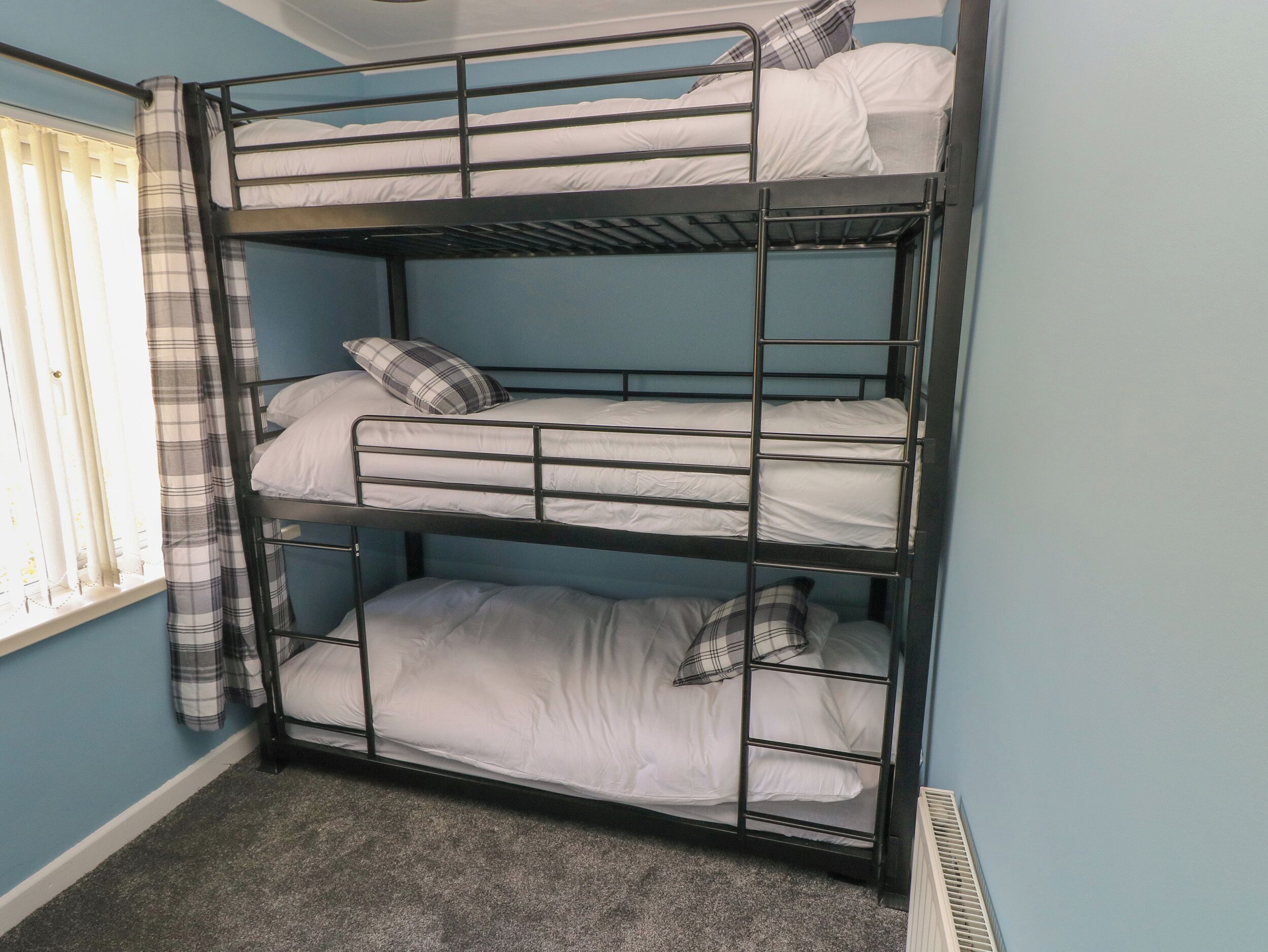 A bunk bed room with three levels, a window with curtains, and a radiator.