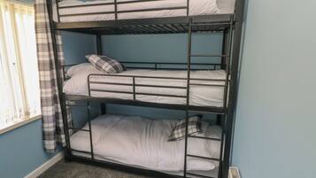 A bunk bed room with three levels, a window with curtains, and a radiator.