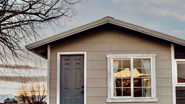 Une maison de plain-pied avec une porte d’entrée, une fenêtre à cadre blanc et un banc à l’extérieur.