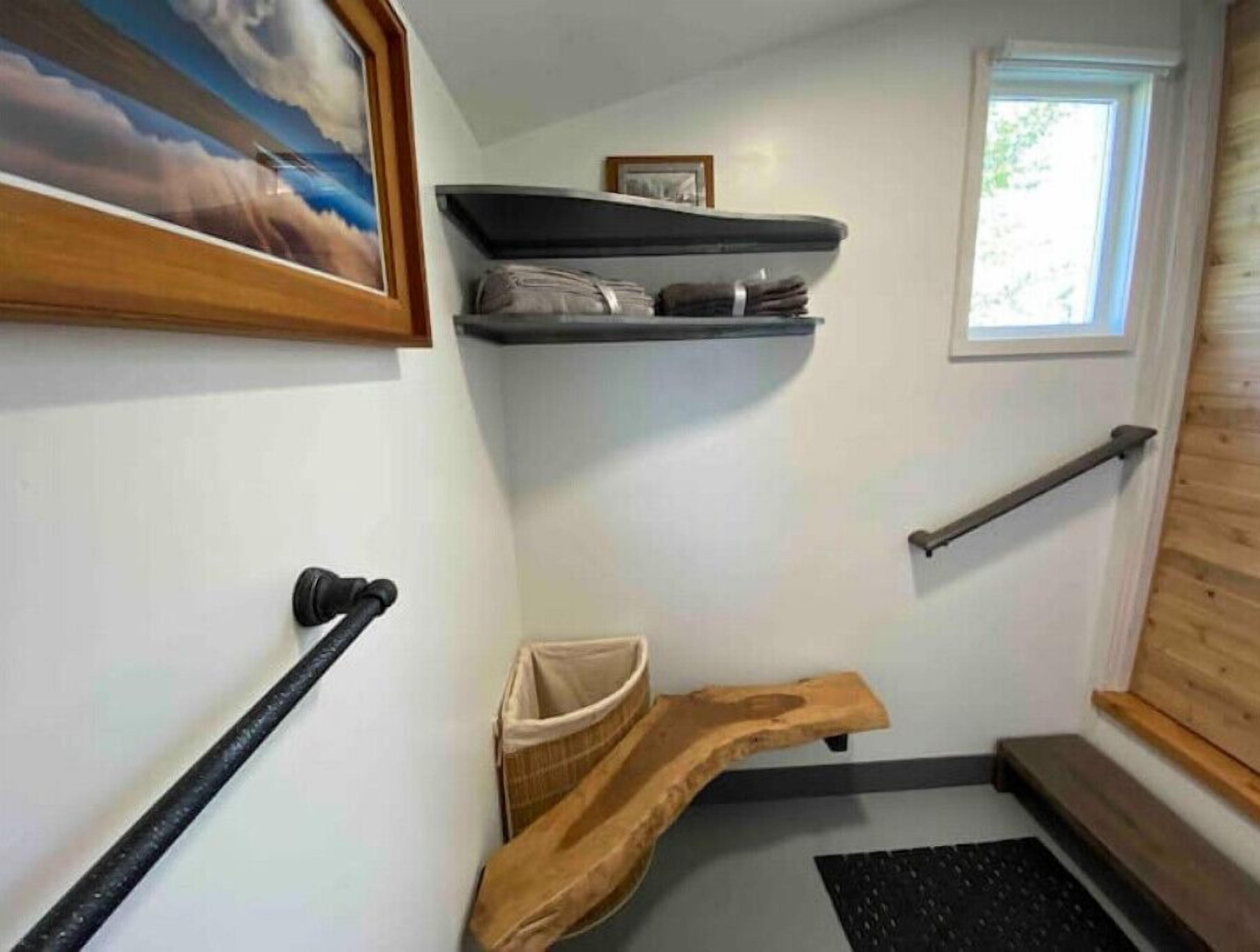 A hallway with a wooden bench, a black handrail, and a window with a view of trees.