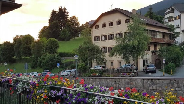A multi-story building with a stone facade, surrounded by lush greenery and parked cars. - ATI Chalet-style apartment from the 1800s in the heart of Ortisei (Ortisei)