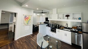 A modern kitchen with white cabinets, stainless steel appliances, and a dining area with a glass table and chairs. - Unit 2_Expansive Luxury Suite for up to 4 Persons (Charlottesville)