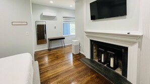A modern living room with hardwood flooring, a fireplace, a mounted TV, and a dining area with a table and chairs. - Unit 2_Expansive Luxury Suite for up to 4 Persons (Charlottesville)