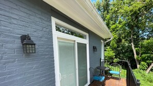 A house with a grey exterior, a sliding glass door, a wooden deck, and a small outdoor seating area with a table and chairs.