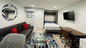 Ein kleines Hotelzimmer mit Sofa, Bett, Schreibtisch, Fernseher und Spiegel.