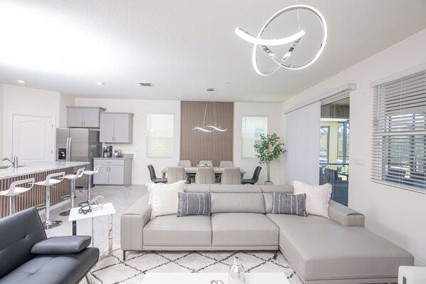 A modern living room with a sofa, coffee table, and a dining area in the background.