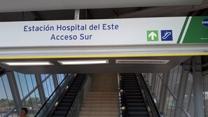 Una escalera mecánica con un cartel que indica 'Estación Hospital del Este Acceso Sur' y flechas direccionales para el acceso.