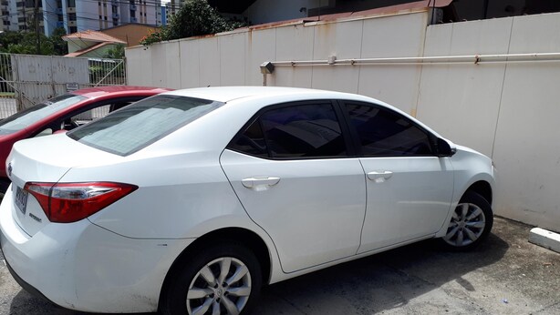 A white sedan parked in an urban area with a concrete ground and a white wall in the background. - Balboa Village (Panamá)