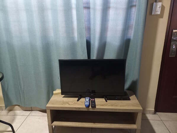 Un televisor sobre un pedestal de madera, con control remoto, toma de corriente y una puerta con cerradura.
