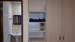 A room with a wooden wardrobe, a white pedestal sink, and a small shelf with folded towels. - Balboa Village (Panamá)