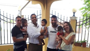 A group of people standing on a concrete patio with a yellow wall and metal fence in the background. - Balboa Village (Panamá)