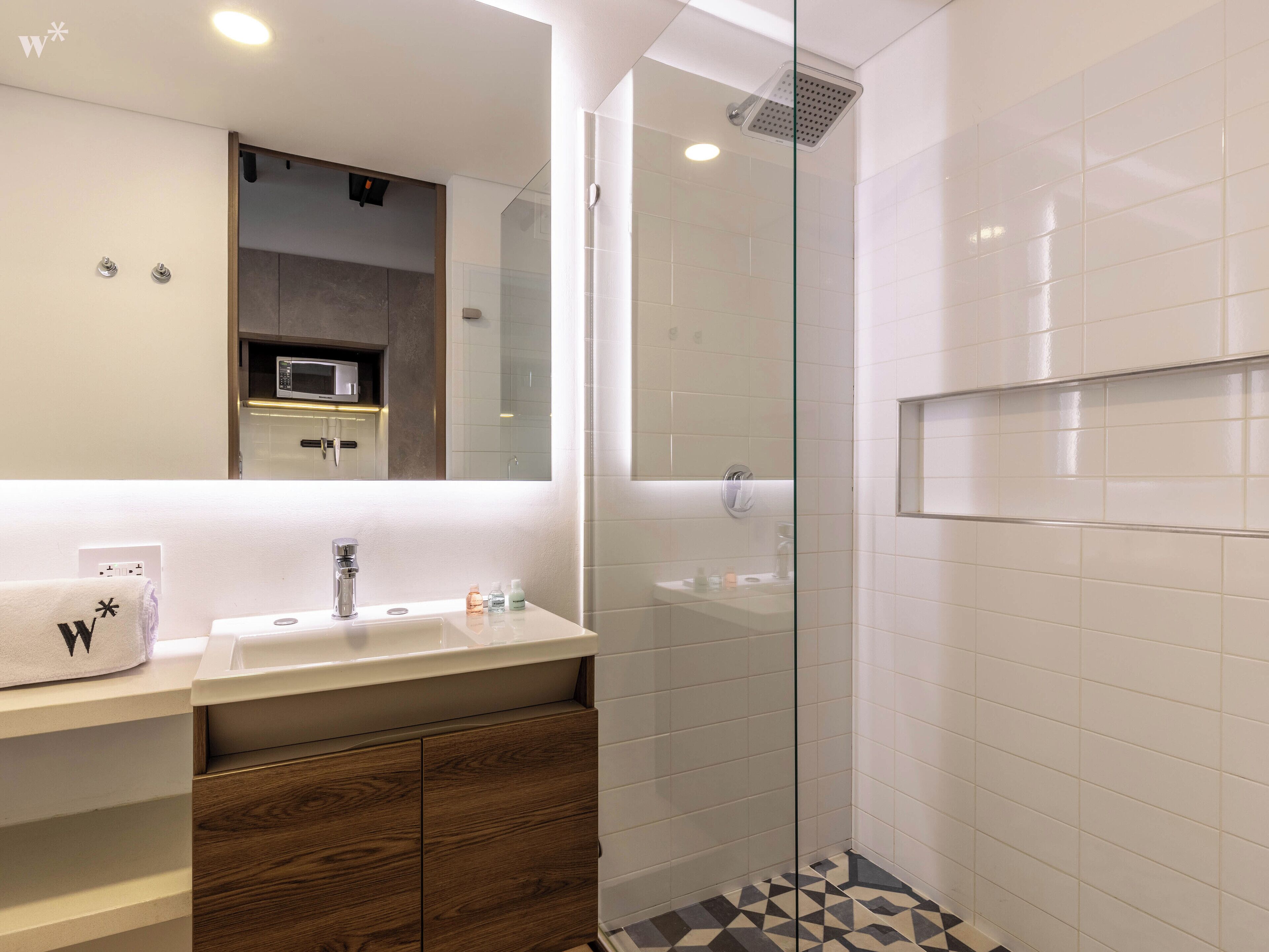 Une salle de bain moderne avec une douche à parois de verre, un lavabo blanc avec un miroir au-dessus et un meuble en bois en dessous.
