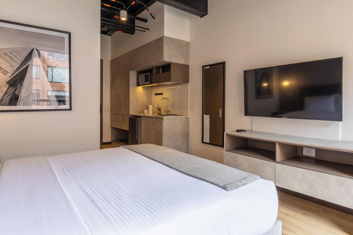 Una habitación de hotel moderna con una cama grande, televisión de pantalla plana, kitchenette y vista panorámica de la ciudad.