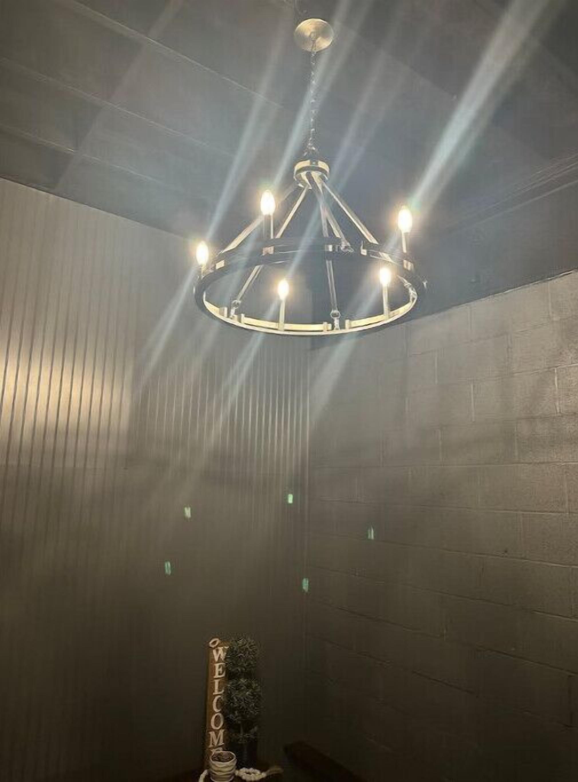 Un lustre composé de plusieurs ampoules suspendues à un point central, une enseigne indiquant « BIENVENUE » et une petite plante posée sur le sol.