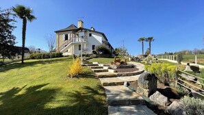 Une maison à deux étages avec un chemin de pierre menant à une terrasse circulaire également en pierre.