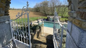Un arc en pierre mène à un espace piscine, d’où l’on peut admirer un jardin aménagé et des arbres.