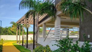 A covered outdoor area with a concrete walkway, palm trees, and a staircase leading to a balcony. - Lofts 1B/R Lounge w/WiFi|Gym|near National Stadium (Kingston)