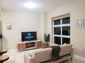 Una sala de estar con un televisor mostrando el logotipo de 'soshomes', un sofá, una mesita y una ventana con persianas.