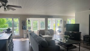 A spacious living room with a sofa, coffee table, and television. Large windows provide a view of the outdoors. - Luxury cottage on beautiful lakefront with hot-tub & private bunkie. New to VRBO (Maberley)