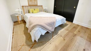 Une chambre à coucher comprenant un lit, des tables de chevet, une lampe, une porte et une œuvre d’art accrochée au mur.