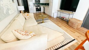 Un salon moderne avec un canapé beige, un téléviseur à écran plat et une cuisine en arrière-plan.