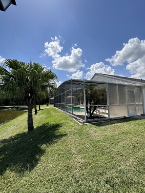 A greenhouse structure with a transparent roof, surrounded by a well-maintained lawn and palm trees.