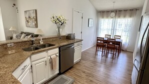 A spacious kitchen with granite countertops, white cabinets, and a dishwasher. There is a dining area with a table and chairs, and a refrigerator in the corner. - Private pool with a beautiful view overlooking the lake! Near Disney & Universal (Kissimmee)