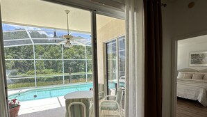 A room with a sliding glass door leading to a pool area, a bed with a headboard, and a ceiling fan. - Private pool with a beautiful view overlooking the lake! Near Disney & Universal (Kissimmee)