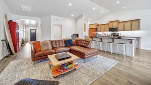 A spacious living room with a sectional sofa, a coffee table, and a kitchen area with wooden cabinets and a bar stool. - New 2 level Twin Falls Home, 2 masters! (Twin Falls)
