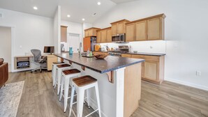 A modern kitchen with wooden cabinets, a large island with bar stools, and built-in appliances. - New 2 level Twin Falls Home, 2 masters! (Twin Falls)