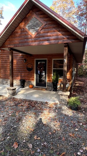 Une cabane en rondins avec des fondations en pierre, une véranda à l’avant dotée d’une balançoire et une cheminée en pierre.