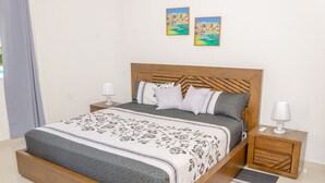 Una cama bien hecha con una colcha estampada y almohadones, flanqueada por mesitas de noche de madera con lámparas, en una habitación de diseño minimalista y limpio.