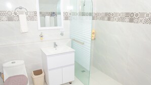 Un baño moderno con un lavabo blanco, inodoro y cabina de ducha con mampara de vidrio.