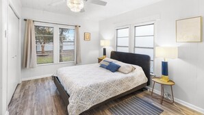 Un dormitorio con una cama, dos lámparas de noche, un ventilador de techo y una ventana con cortinas.