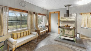 Una habitación acogedora con un banco de madera, una estufa antigua y ventanas grandes con cortinas.