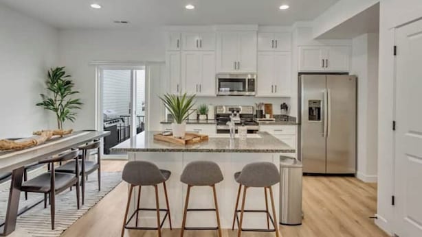 Una cocina moderna con armarios blancos, electrodomésticos de acero inoxidable y una isla central con taburetes de bar.
