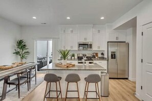 Une cuisine moderne avec des meubles blancs, des appareils en acier inoxydable et un îlot central doté de tabourets de bar.