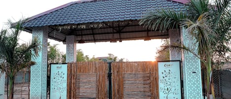 Una entrada techada con techo de tejas, dos puertas de madera con diseños de árboles y una palmera a la derecha.