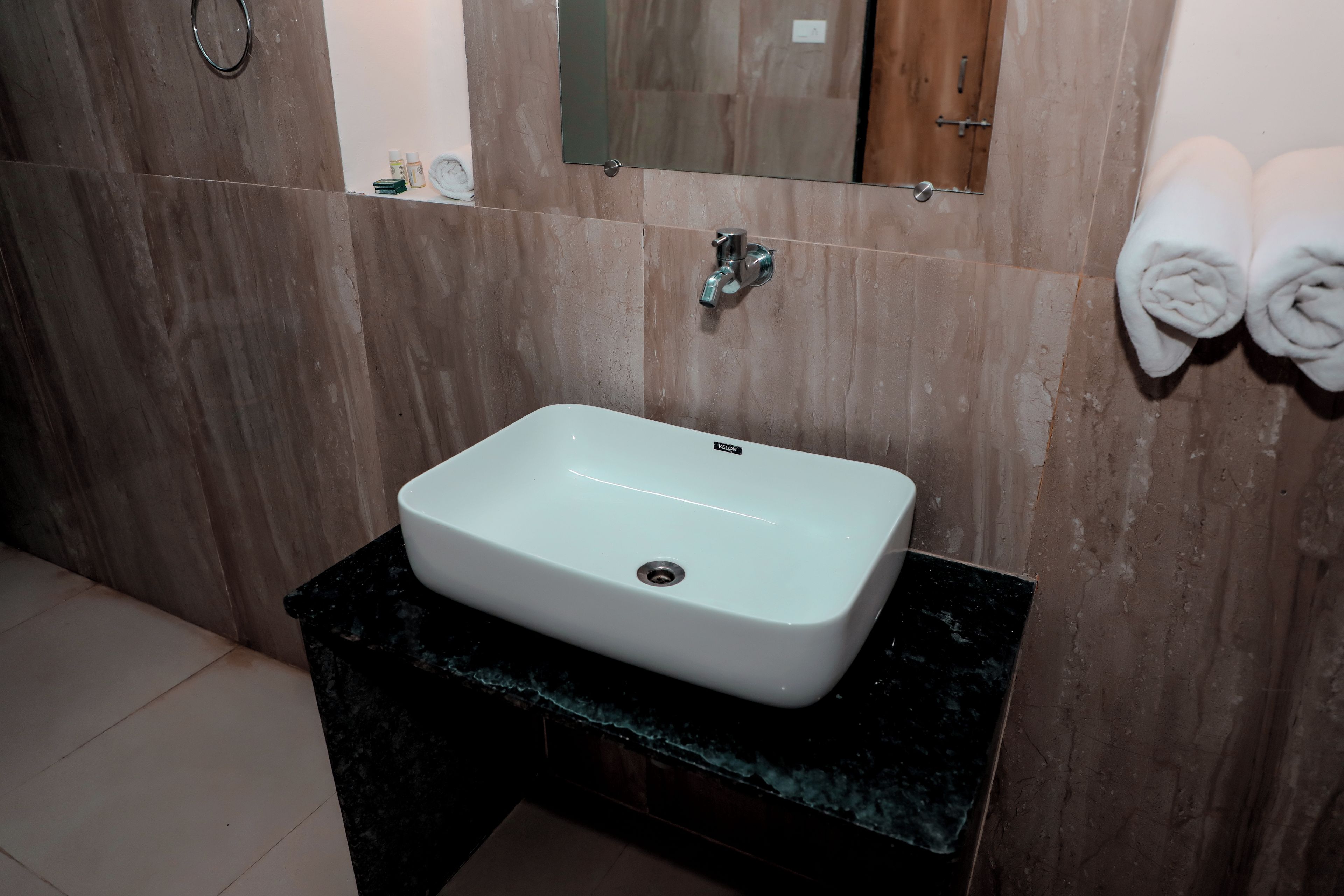 A bathroom with a rectangular sink on a black countertop, a mirror above it, and a towel rack to the right.