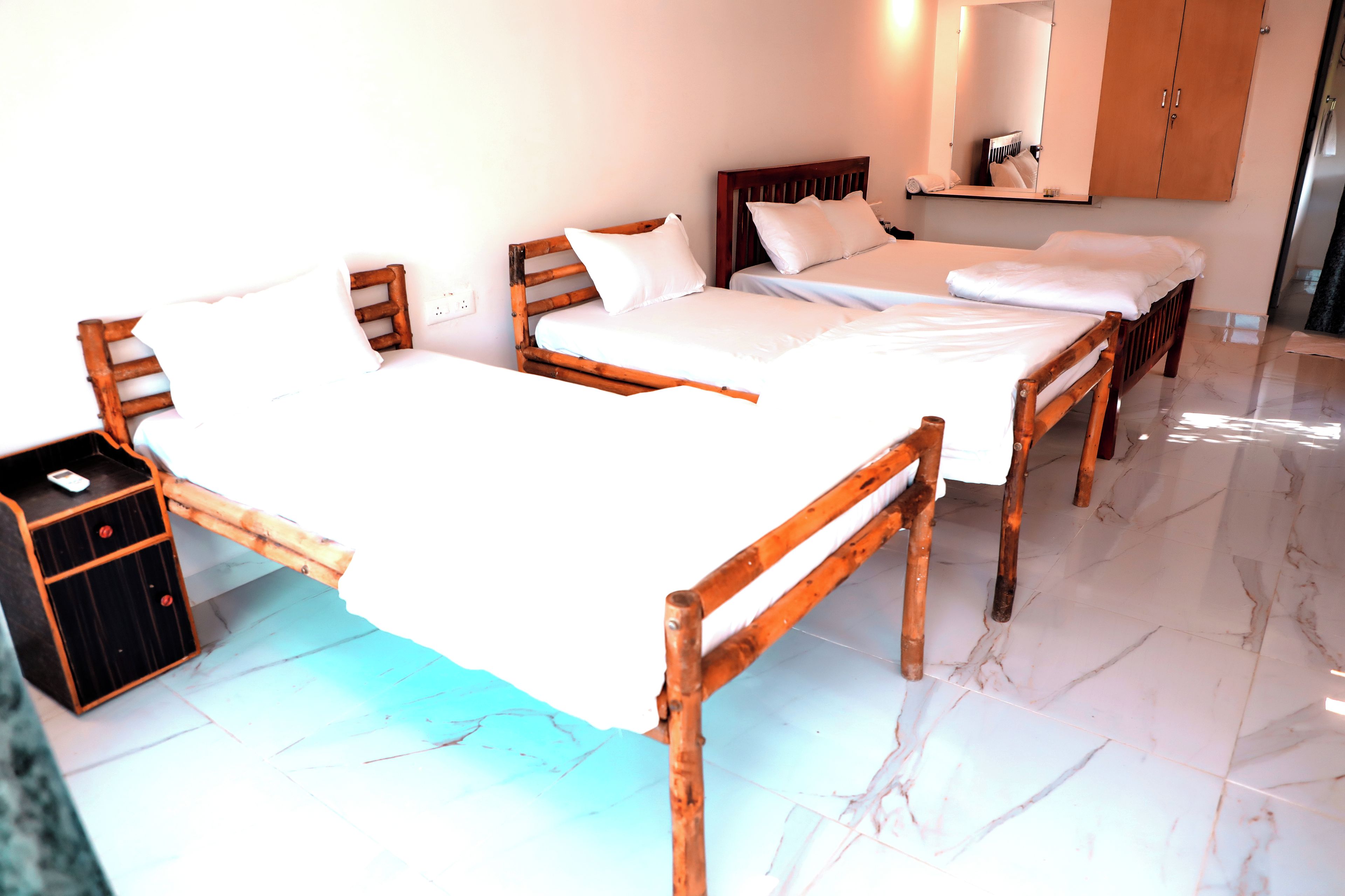 A hotel room with three wooden beds, a nightstand, a mirror, and a wardrobe.