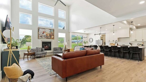A spacious living room with a large brown sofa, a fireplace, and a dining area with bar stools. - Pickleball Playhouse, Hot Tub, Theater, Game Room! (Lava Hot Springs)