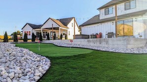 A residential area with a well-maintained lawn, a stone pathway, and houses with large windows and a garage. - Pickleball Playhouse, Hot Tub, Theater, Game Room! (Lava Hot Springs)