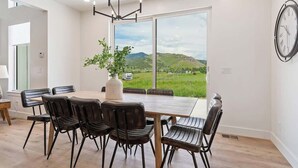 A dining area with a large table and chairs, a potted plant, and a view of a green landscape through large windows. - Pickleball Playhouse, Hot Tub, Theater, Game Room! (Lava Hot Springs)