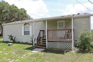 A single-story mobile home with a front porch, a small front yard, and a cactus plant.